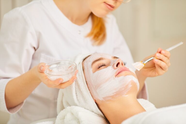 A cosmetologist applies a mask to a woman. A woman is relaxing in the spa salon.